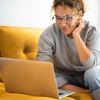 Woman with glasses smiling while looking at laptop