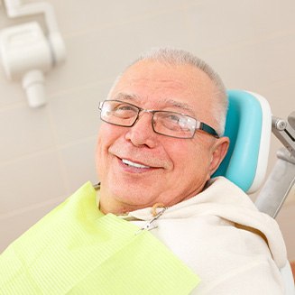 Senior man with glasses sitting in dental chair and smiling