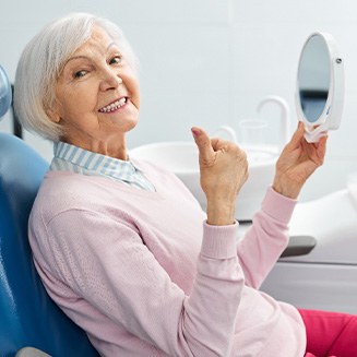 Senior woman checking smile in mirror and giving thumbs up