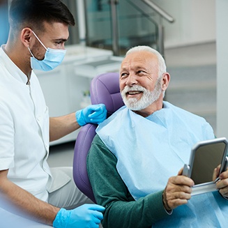 Senior patient looking at dentist while holding small mirror
