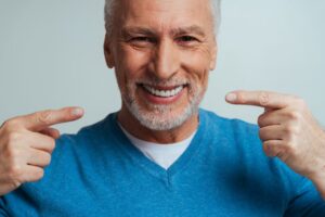 Older man pointing to dentures and smiling. 